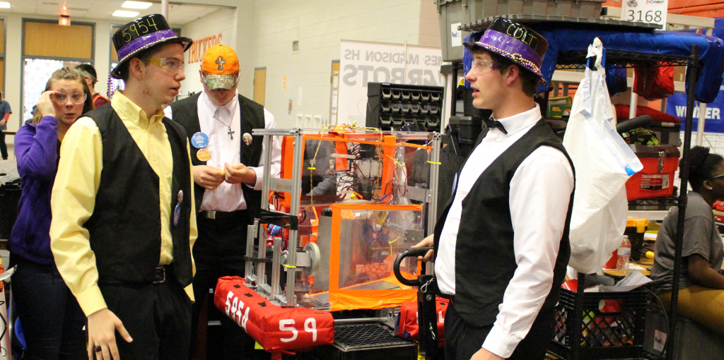 Two men with matching hats in front of a robot.